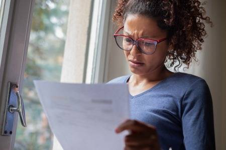 sad-black-woman-near-window-reading-bad-news-letter